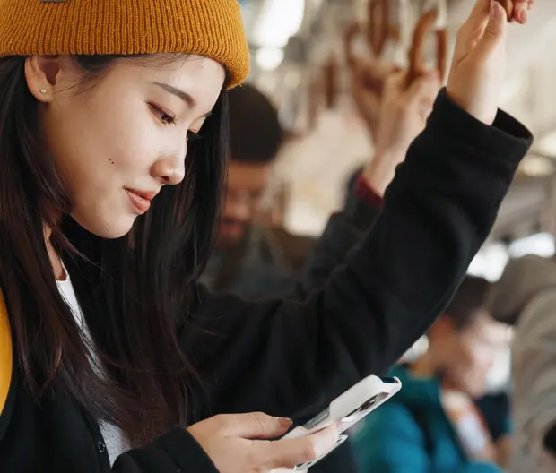 A young woman is looking at her phone while commuting.